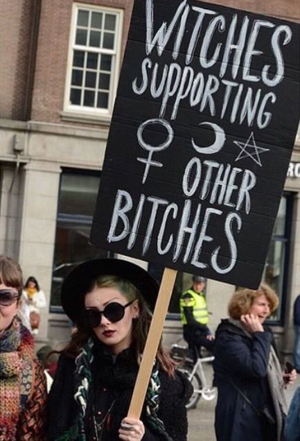a witch holding a black sign in a feminist march