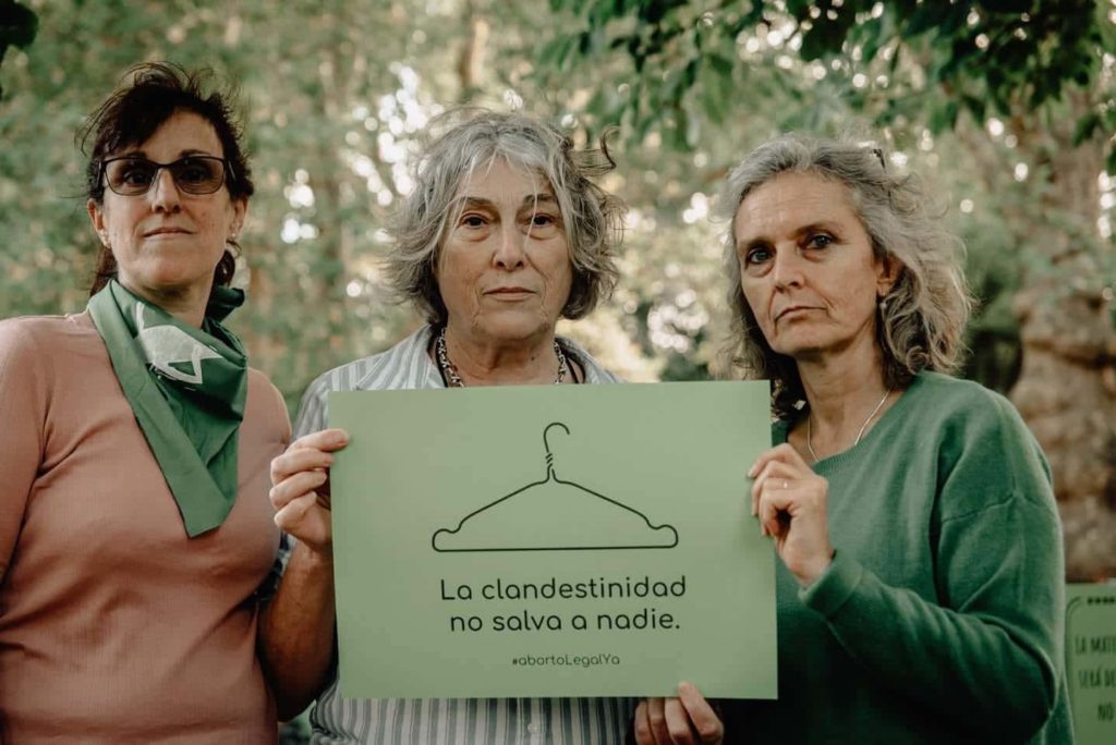 three women together holding a pro abortion sign with the phrase "la clandestinidad no salva a nadie"